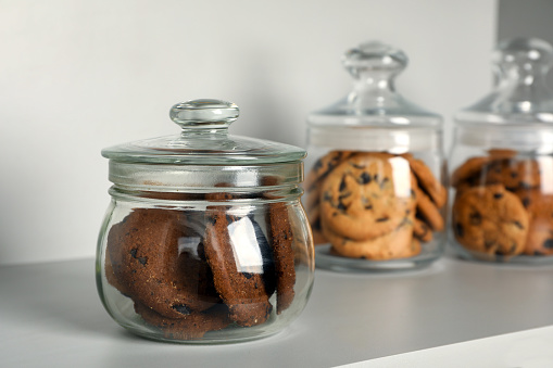 Delicious chocolate chip cookies in glass jars on white table, space for text
