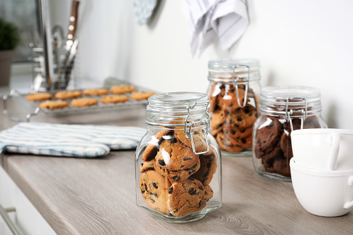 Delicious chocolate chip cookies in glass jars on wooden table in kitchen