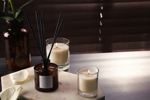 Aromatic reed air freshener and burning candles on white windowsill, space for text