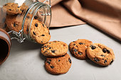 Overturned glass jar with delicious chocolate chip cookies on light grey table, closeup
