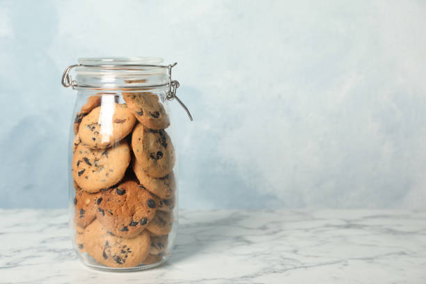 istock Delicious chocolate chip cookies in glass jar on white marble table, space for text 1453136571