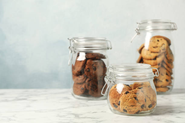istock Delicious chocolate chip cookies in glass jars on white marble table, space for text 1453137234