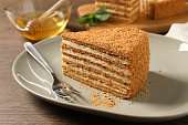 Slice of delicious layered honey cake served on wooden table, closeup