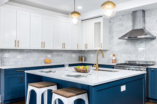 A luxurious white and blue kitchen with gold hardware, stainless steel appliances, and white marbled granite countertops.