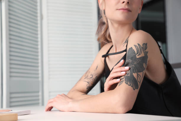 bella donna con i tatuaggi sul corpo al tavolo all'interno, primo piano - tattoo women bird shoulder foto e immagini stock