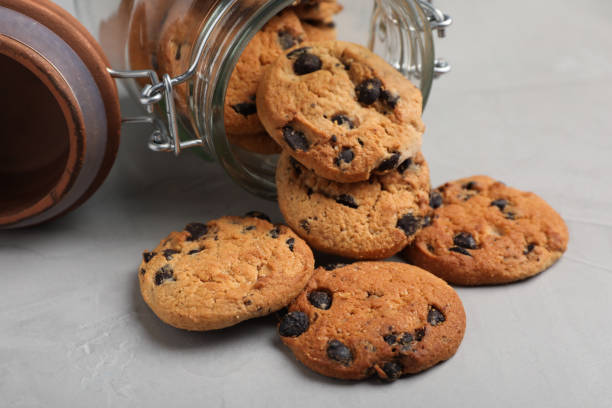 istock Overturned glass jar with delicious chocolate chip cookies on light grey table, closeup 1453138183