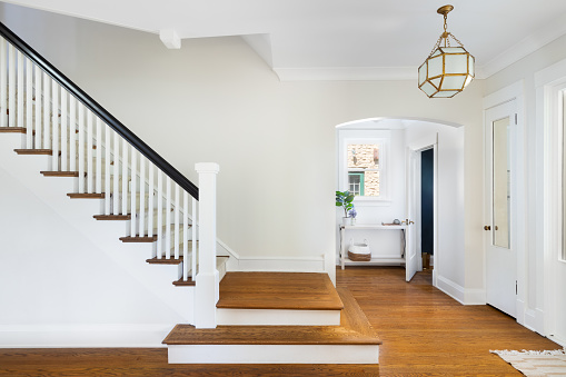 A renovated stairway in the home's foyer with a view of a mud room and doorway to a small, blue bathroom. A modern light hangs above the hardwood floors.