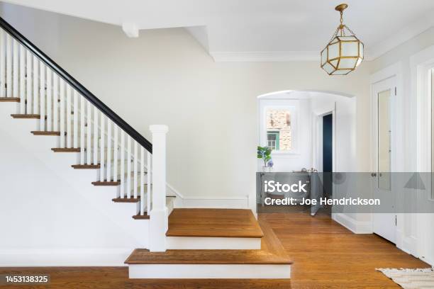 A Homes Foyer With A Renovated Staircase And Gold Light Fixture Hanging Above Stock Photo - Download Image Now