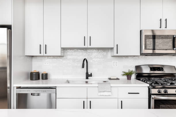 A white kitchen detail shot with a black faucet and tiled backsplash. A beautiful white kitchen detail shot with a tiled backsplash, white cabinets, stainless steel appliances, and black hardware and faucet. kitchen dishwasher stock pictures, royalty-free photos & images