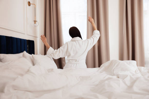 istock Young woman wearing bathrobe waking up in hotel room, back view 1453138355