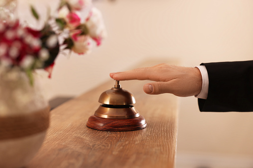Man ringing service bell at wooden reception desk in hotel, closeup