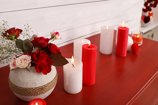 Burning candles and vase with flowers on red table indoors. Valentine's Day celebration
