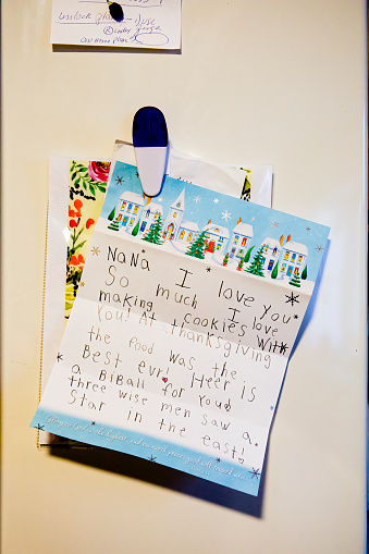Modern refrigerator door with child's notes and magnets in kitchen, close up.