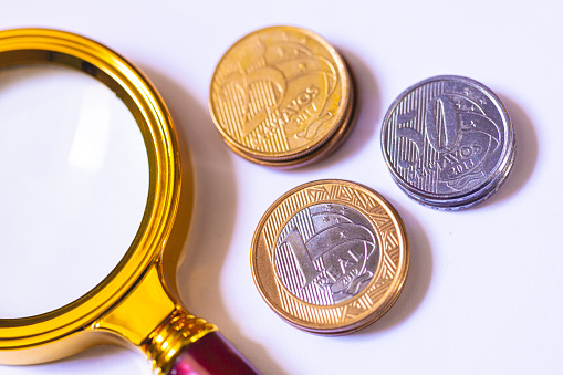 Brazilian Real coins and a magnifying glass. Brazilian economy, finance and inflation.