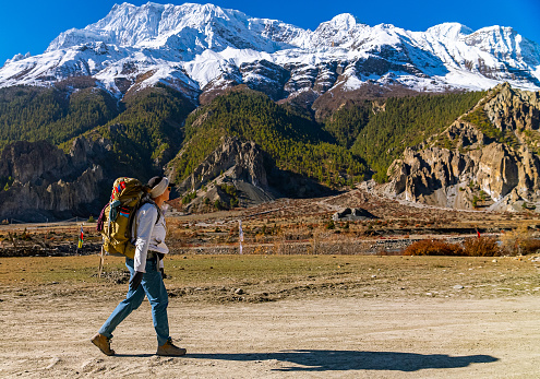 Female trekker walking along a footpath with a large mountain range with snowy peaks in the distance on the Annapurna Circuit trek