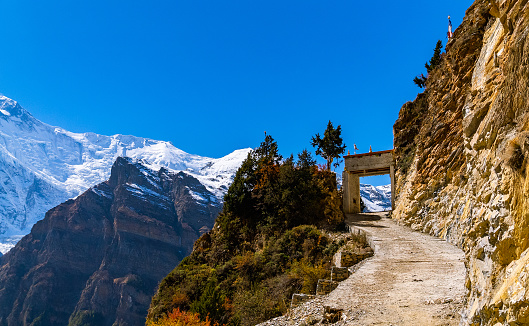 Trail by the snowy himalayan mountains on the Annapurna Circuit Trek, Nepal. Sunny cloudless sky bringing calmness