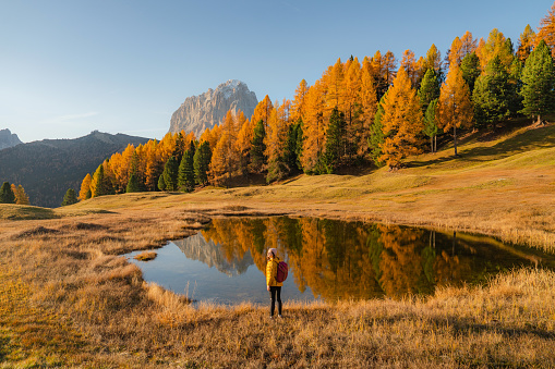 Young Caucasian woman in yellow jacket  hiking on the background of the lake in Dolomites in autumn