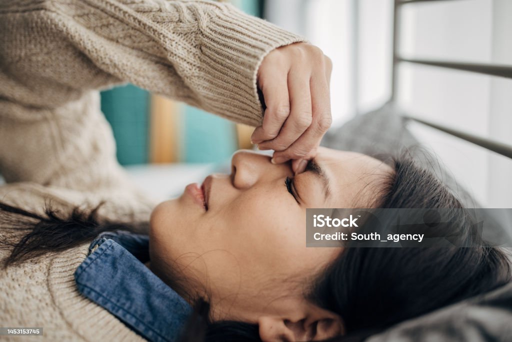 Problems with headache One woman, Japanese woman having headache while lying on bed in her bedroom at home. Headache Stock Photo
