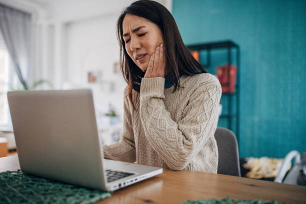 Toothache is a problem One woman, Japanese woman having toothache while working on laptop in her home office. toothache stock pictures, royalty-free photos & images