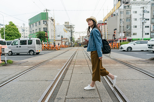 full length with side view asian female traveler passing by railroad crossing in downtown Osaka, japan in spring at daytime