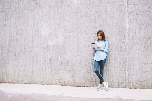 istock Millennial hipster girl touching with finger on screen of modern touch pad while networking online, woman holding digital tablet device for reading web news standing at city publicity area 1453155970