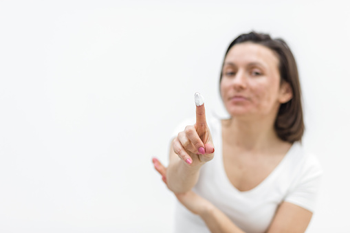 Photo of positive woman holding a cream in hand on white background. Concept of skin care.