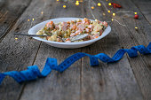 The concept of overeating and losing weight after the Christmas holidays. Measuring tape and a plate with olevier salad against the background of New Year's lights on a wooden background.