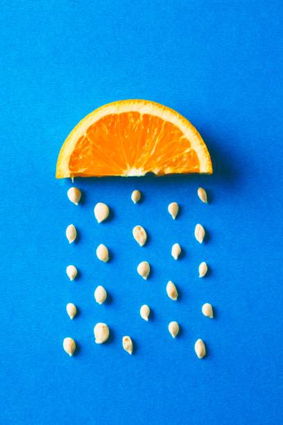 istock Creative food concept with an orange slice and seeds falling down like raindrops on blue background 1453158903