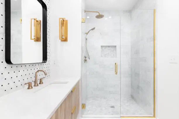 Photo of A bathroom with gold faucets and a shower lined with marble tiles.