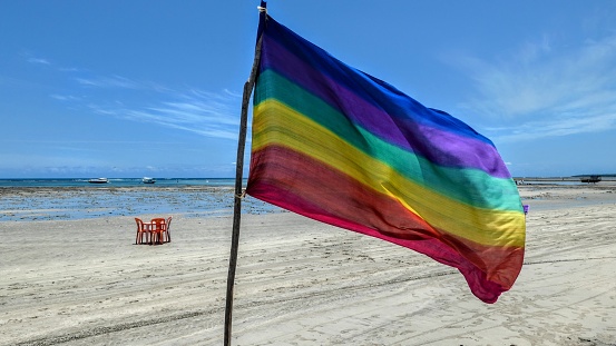 A closeup shot of a Rainbow flag on the beach in Morro de Sao Paulo, Brazil with a blue sky behind