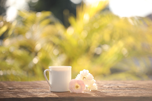 White coffee mug and roses on wooden table outdoor