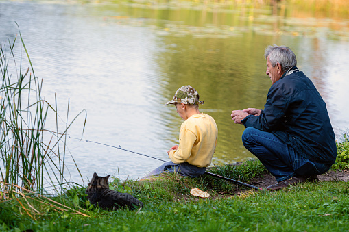 Riga, Latvia, September 12, 2020: a grandfather with a boy and a cat is sitting by the river and fishing