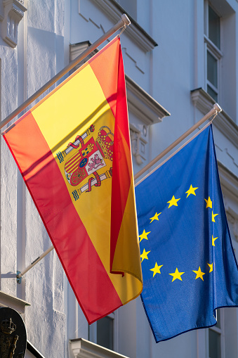 Backlit Spanish flag hanging along with flag of EU in front of old house in Bratislava