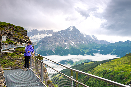 Senior woman enjoying the Cliff walk on First (pronounced Feerst) high above Grindelwald in the Swiss Alps with breathtaking views of the Eiger, Mönch, and Jungfrau mountain range