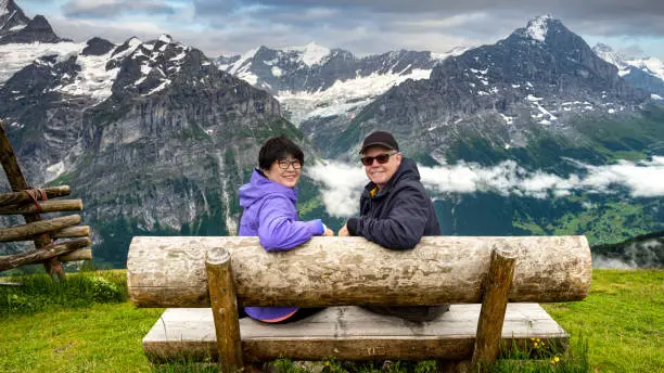 Senior couple sitting on wood bench enjoying the view at the top of First (pronounced Feerst)  mountain in Grindelwald, Switzerland.
