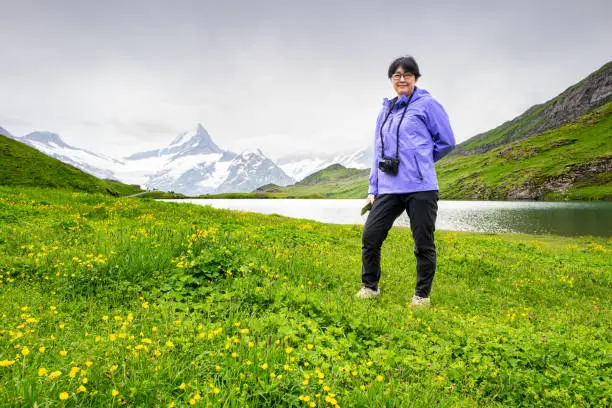 Senior Korean woman hiking near Bachsee lake with Swiss alps in the background on a cloudy misty summer day.