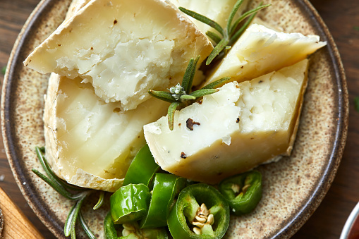 A top view of parmesan or goat cheese with truffles, green hot pepper and rosemary, pieces and crumbs in a handmade ceramic bowl, on a wooden cutting board, an image with a copy space