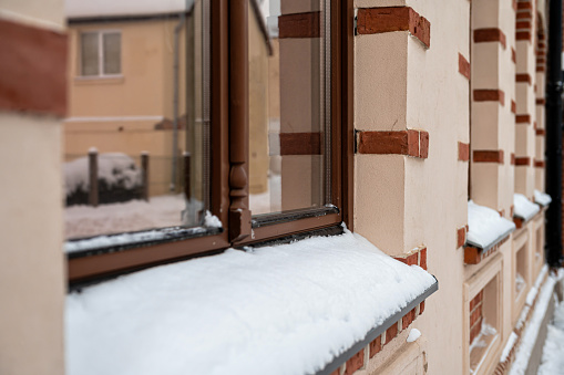 Window sill covered with heavy snow in winter, close-up of building facades and window