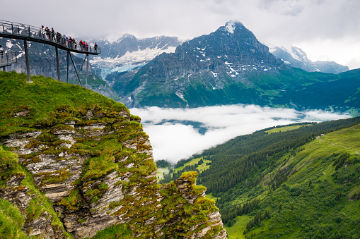 Grindelwald, Switzerland - June 28, 2022: Tourist and hikers enjoy the view from the cliff walk metal bridge on the top of First ( pronounced Feerst ) in the Swiss Alps above the cloud cover over Grindelwald Switzerland.