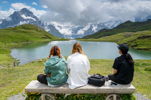 Grindelwald, Switzerland - June30, 2022: Young tourists sitting on park bench enjoying the view of the Swiss Alps near Bachalpsee