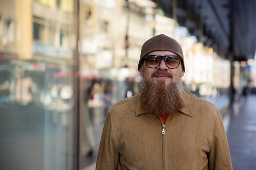 Headshot of urban mid-adult Caucasian man with long beard, in the city