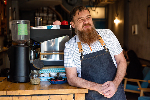 Portrait of urban mid-adult Caucasian man, an small business owner, wearing apron, while standing at coffee shop