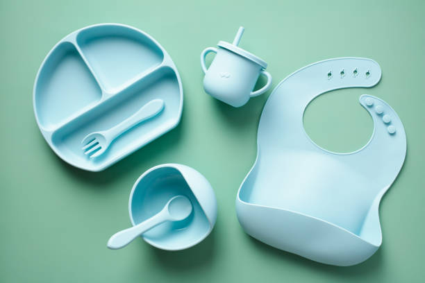 istock Silicone tableware set on color background. Flat lay baby bib, bowl with spoon, fork, cup. Baby feeding concept. 1453182468