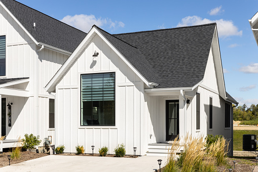 Elmhurst, IL, USA - September 25, 2022: A small, ranch style modern farmhouse with white vertical siding, black roof, large front window, and black front door.