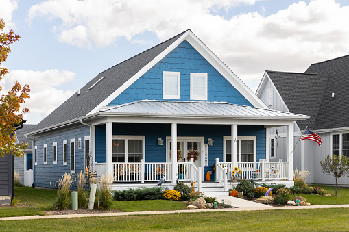 Elmhurst, IL, USA - September 25, 2022: A large, two story farmhouse with vibrant blue siding and white covered front porch.