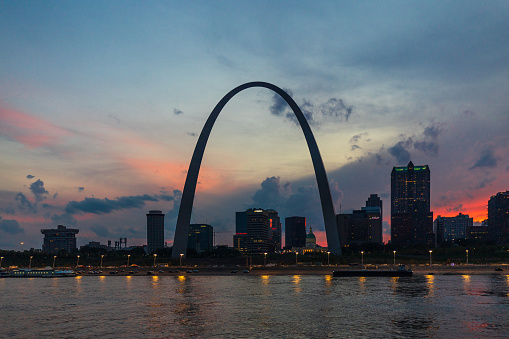 St. Louis, MO, USA - August 10, 2018: A view from the Mississippi River of a dark St. Louis skyline with the Gateway Arch. A sunset/sunrise, after a rainstorm, lights up the sky with colorful clouds.