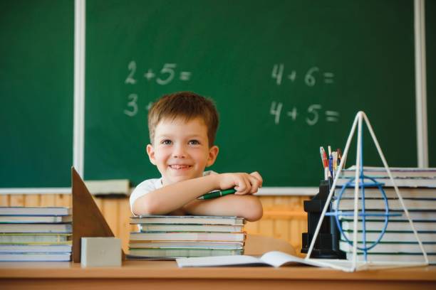 istock Back to school. A schoolboy is reading a book while sitting at the table for the first time at school on the background of the school blackboard. 1453186286