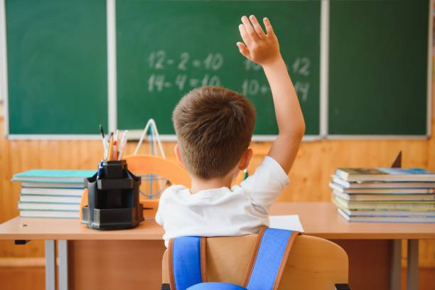 Elementary students raise hands during a school lesson. Concept of education, curiosity, and active learning in a multicultural environment.