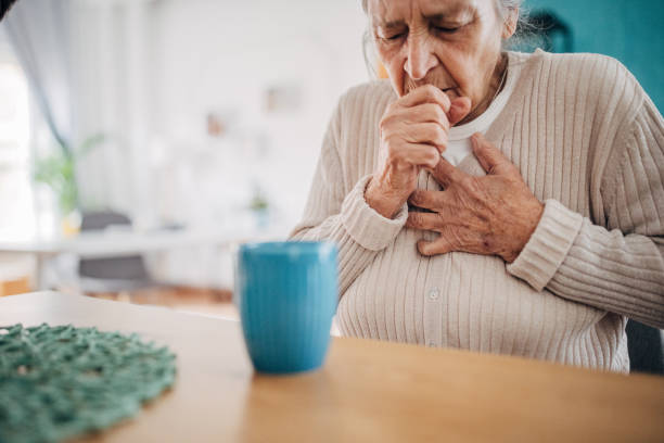 Old woman coughing One woman, old woman coughing and touching her chest from her flu, while sitting at home. one senior woman only stock pictures, royalty-free photos & images