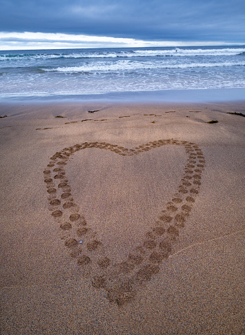 Drawing of a heart on the sand and wave with foam